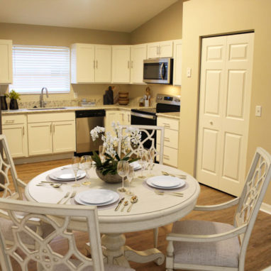 Round white dining table and chairs with kitchen in the background.