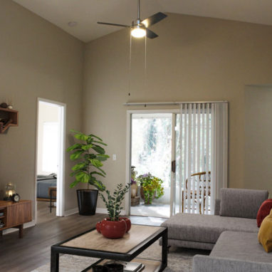 A furnished living room with vaulted ceilings and a glass door leading out to a patio.